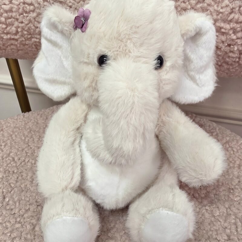 Elefantita de peluche marfil con florecita lila junto a la oreja