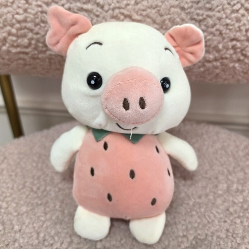 Cerdito de peluche blanco con disfraz de fresa rosada y cuello de hojas verdes
