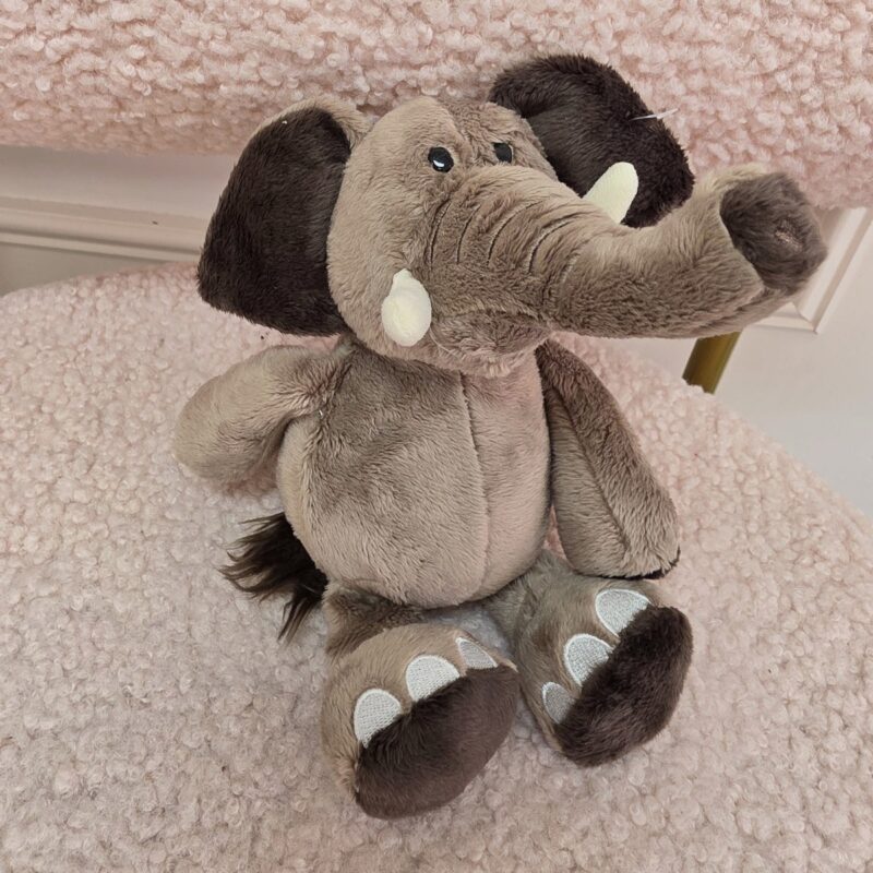 Elefante de peluche gris con colmillos marfil y trompa enrollada