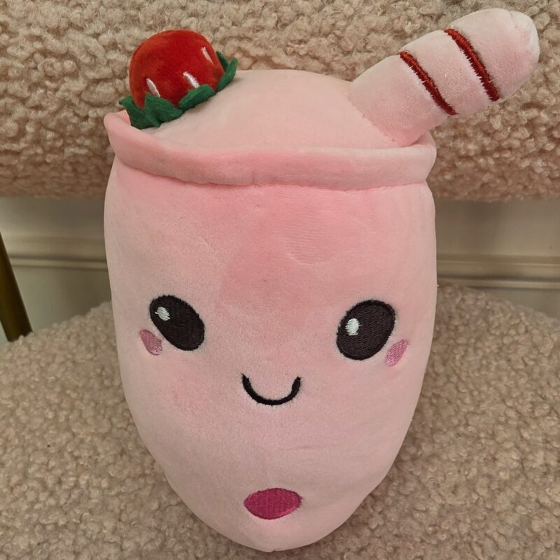 Peluche rosado de batido de fresa con carita sonriente, pajita y fresa