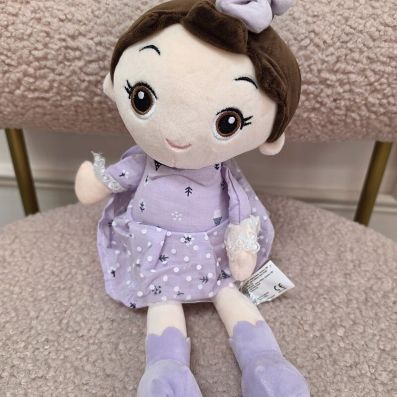 Muñeca de peluche de cabello café con vestido lila, puños de encaje y moño lila