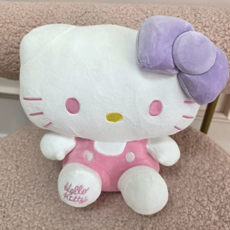Peluche Hello Kitty con moño lila, overol rosado y Hello Kitty bordado en el pie