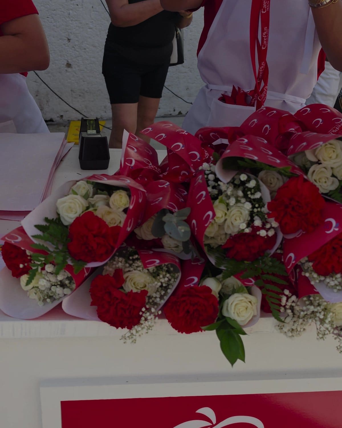 Ramitos de claveles rojos y rosas blancas en papel impreso con el logo de CarePlus sobre el carrito