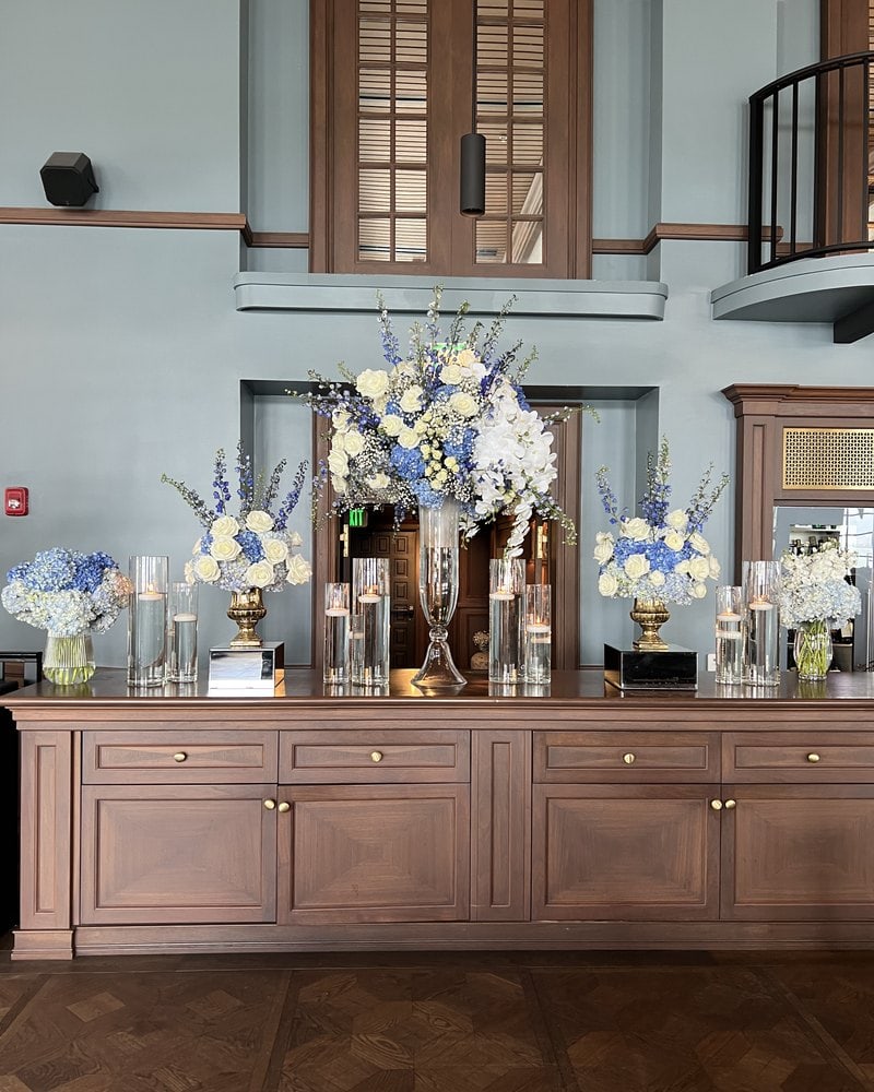 Tall white and blue centerpieces on a wooden credenza for a reception