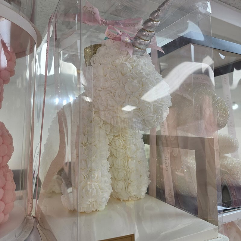 Unicornio de rosas de espuma marfil con cuerno plateado y cinta rosada en caja transparente