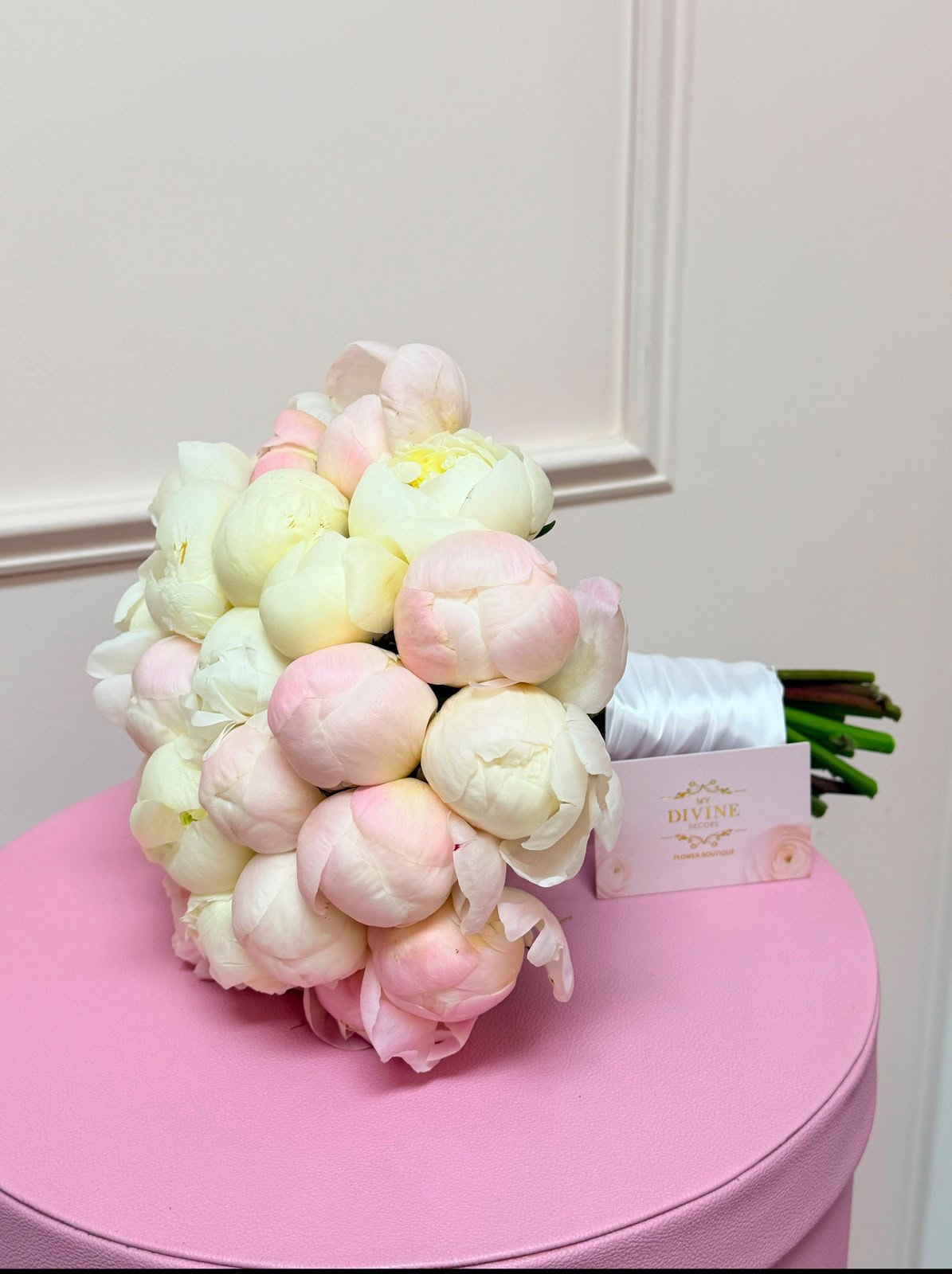 Ramo de Novia de Peonías Blush de My Divine Decors con la cinta atada a mano sobre un pedestal rosado
