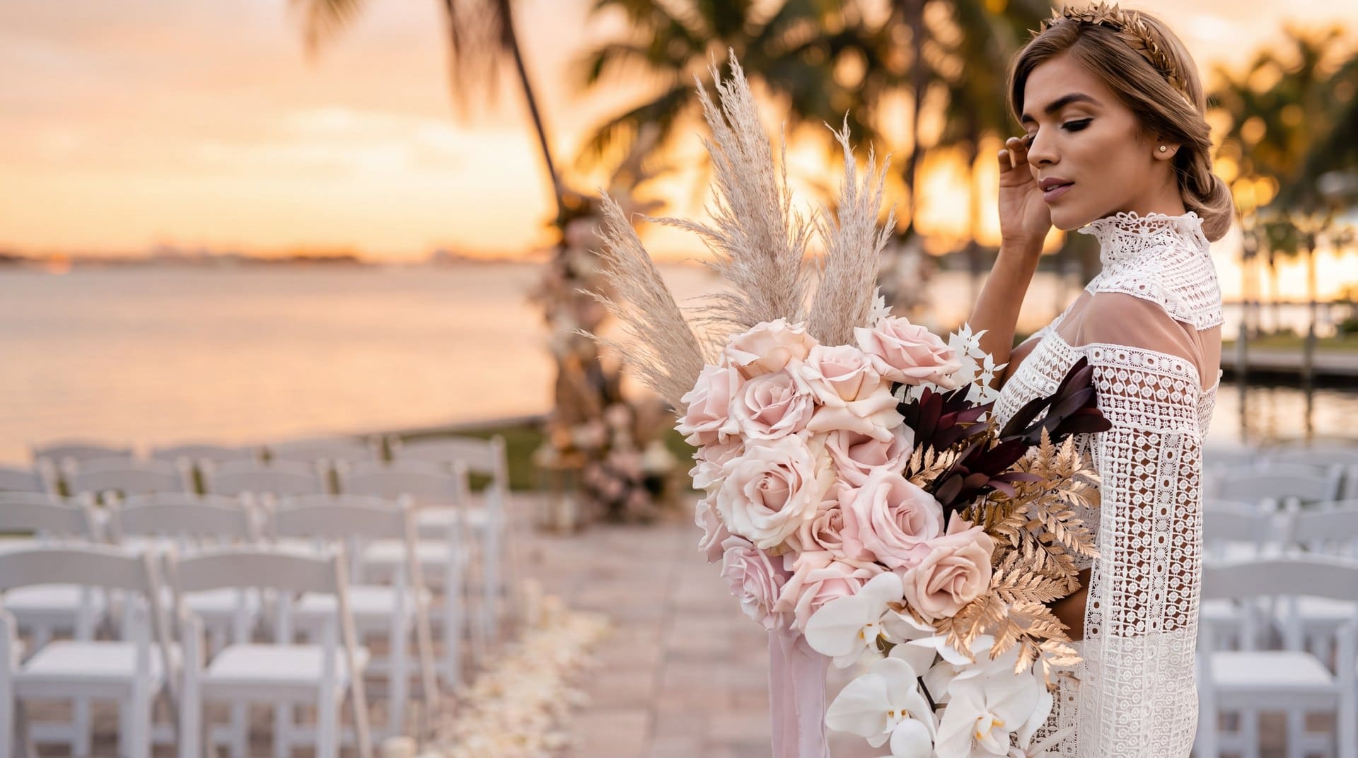 Bride in a white crochet lace gown holding a cascading bouquet of blush roses, white orchids and pampas by My Divine Decors at a waterfront wedding venue in Miami at sunset
